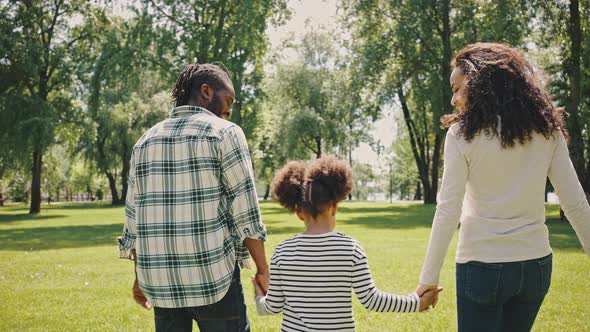 Rear View of Happy Mixed Race Family Parents with Cute Child Girl Holding Hands and Walking Together