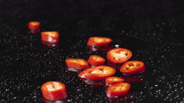 Slices of Red Hot Chili Pepper Falling on Wet Black Surface