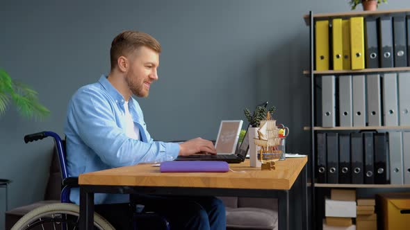 Motivated Disabled Person Freelancer is Working with Laptop Typing Sitting in Wheelchair at Office