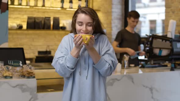 Portrait of Young Beautiful Caucasian Woman Smelling Hot Fresh Coffee and Smiling at Camera