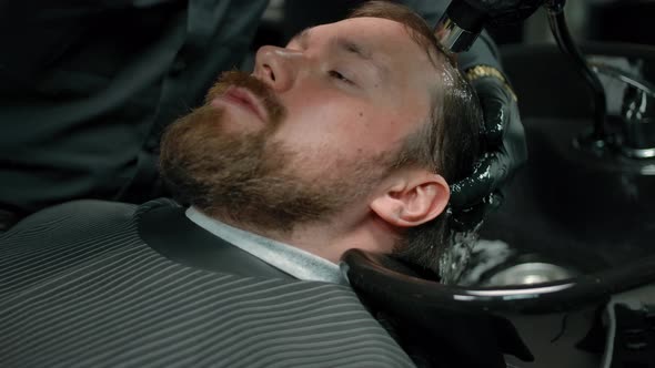 The Head of a Bearded Man is Washed with Shampoo Foam in a Barbershop
