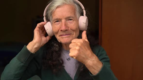 Very Elderly Woman Village Pensioner Listens to Music with Wireless Headphones