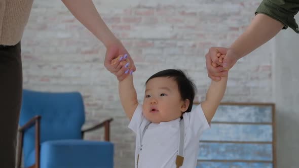 Asian toddler close-up holds hands of parents and takes first steps