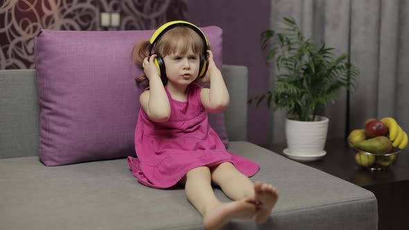 Little Child Girl in Headphones Enjoying Listen Music. Dancing on Sofa at Home