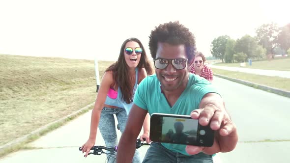 Three young adults having fun cycling and taking selfies, graded