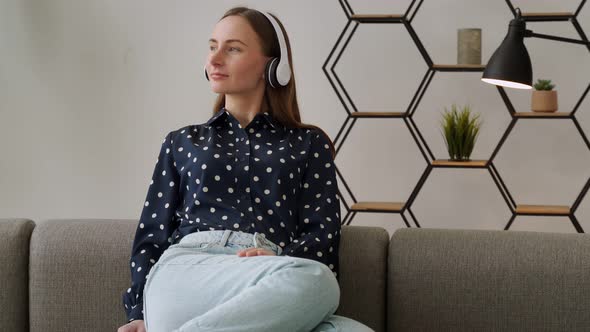 Relaxed Young Woman is Sitting on the Couch Enjoying Music Through Headphones From a Smartphone at