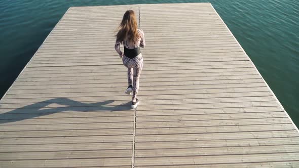 Girl athlete with a beautiful figure runs on the pier of the lake. Slow motion. Top view.