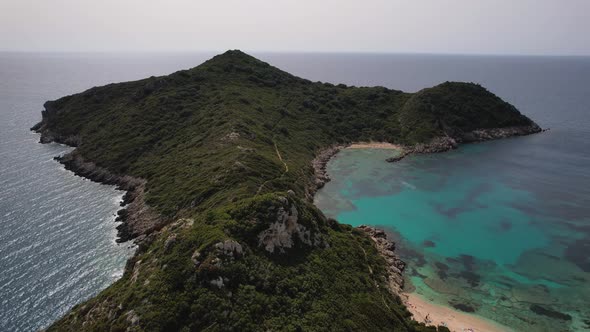 Forward shot over green Island surrounded by blue water and white beaches. Small tracking path along