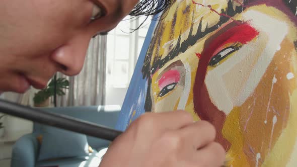 Close Up Of An Asian Artist Man Holding Paintbrush And Painting A Girl's Face On The Canvas