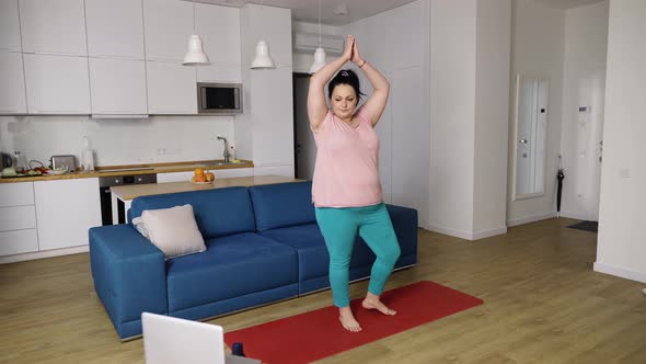 Plump Woman Performing Yoga Asana at Home with Online Tutor on Laptop