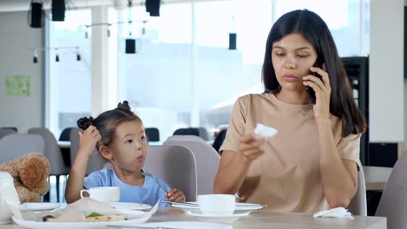 Businesswoman Cleans Kid Mouth Talking on Smartphone in Cafe