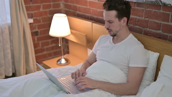 Young Man Having Coughing While Working on Laptop in Bed