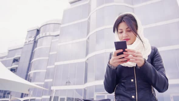 Young Brunette Woman Sits Outside with Her Phone