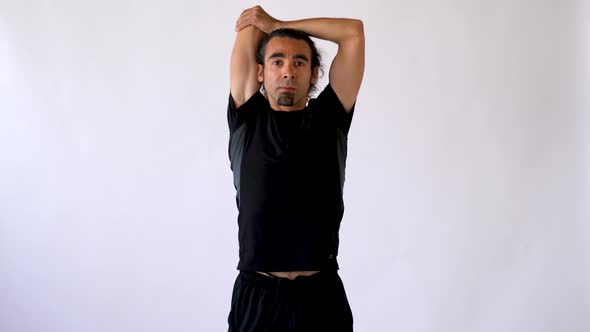 Hispanic Man with Long Hair and Goatee Performing Tricep Stretch Against White Studio Backdrop