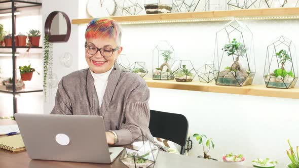 Mature Modern Business Lady Looking at Screen of Laptop Smile While Typing To Colleague