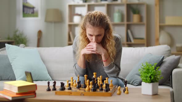 Young Woman Learn to Play Chess Online with Video Tutorials at Home in Living Room