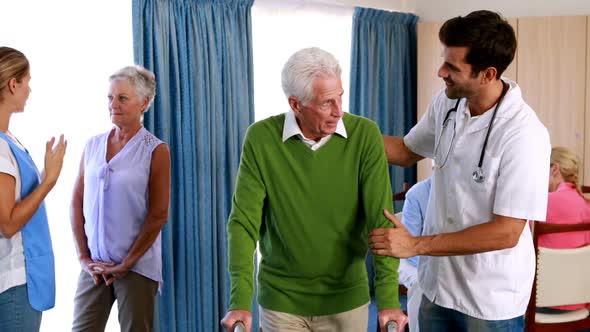 Doctor assisting seniorman to walk with walker