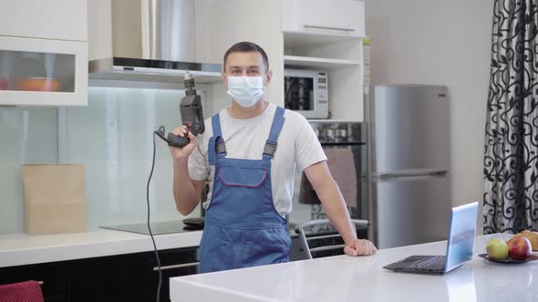 Positive Confident Repair Man in Covid19 Face Mask Posing with Electric Tool in Apartment