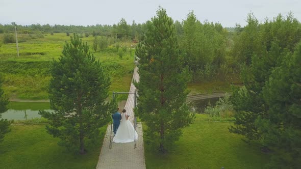 Newlywed Couple Walks To Wooden Bridge Aerial Backside View