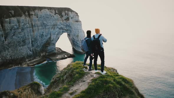 Drone Moving Around Young Happy Friends Standing Together on Top of Sunset White Coast Cliff