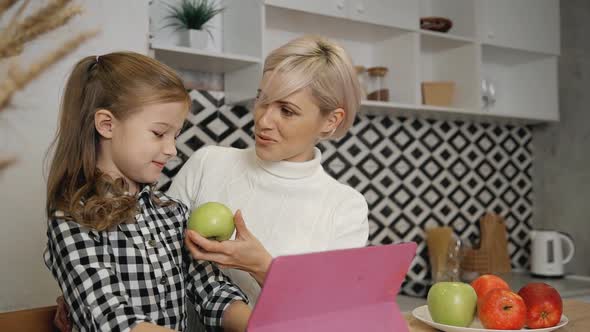 Mother Giving Green Apple To Daughter in Kitchen.