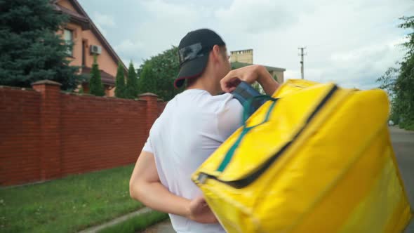 Live Camera Follows Yellow Delivery Bag As Young Man Putting on Backpack Walking