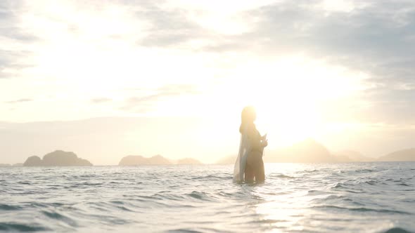 Woman In Bikini And Sun Hat Standing In Sea At Sunset