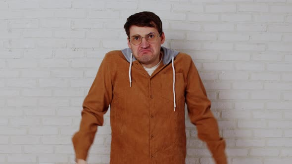 Young Man in Glasses Spreading Hands on Background of White Brick Wall