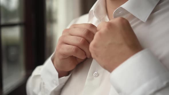 Man Buttons Up His White Shirt Standing in the Front of a Bright Window