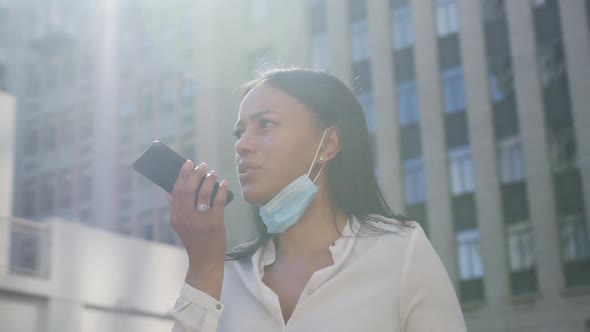 African american woman wearing face mask talking on smartphone in city street