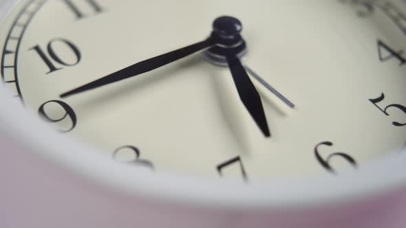 Classic alarm clock with a white dial and black arrows on a pink background 