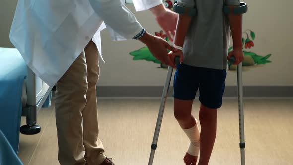 Male doctor assisting injured boy to walk with crutches