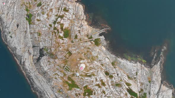 Ultra wide bird's eye view pan of isolated red and white stone lighthouse on top of a white craggy s