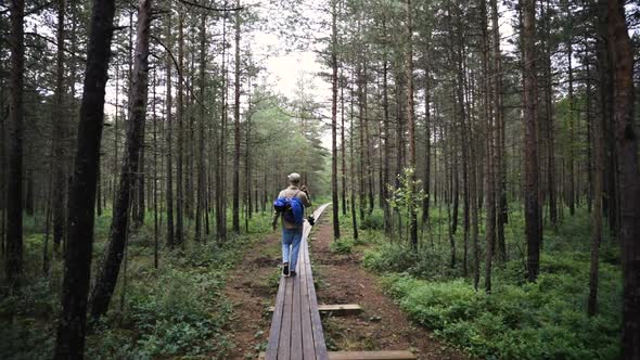 Follow shot of young man with camera walking through forest on planks