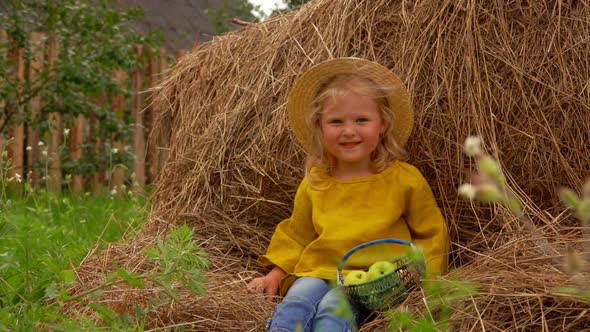 Cute Girl Sits on a Haystack with a Basket