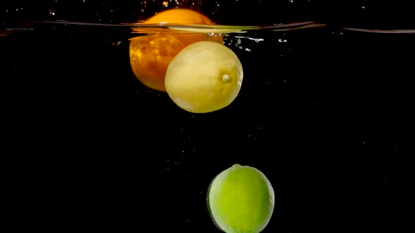 Colorful citrus fruits being dropped into water in slow motion.
