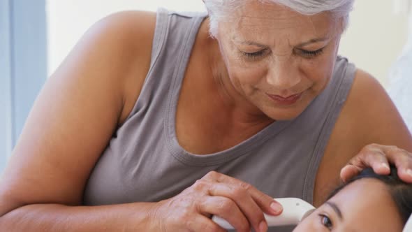 Grandmother checking body temperature of sick granddaughter in bed room