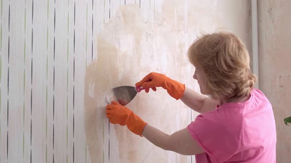 An Adult Woman Takes Off the Wallpaper Works with a Spatula in the Room