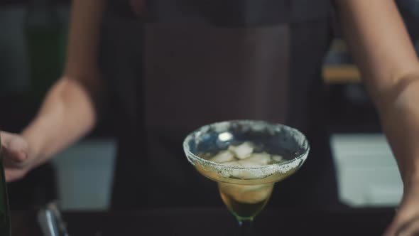 Close up of bartender pouring tequila into margarita glass with a lime.