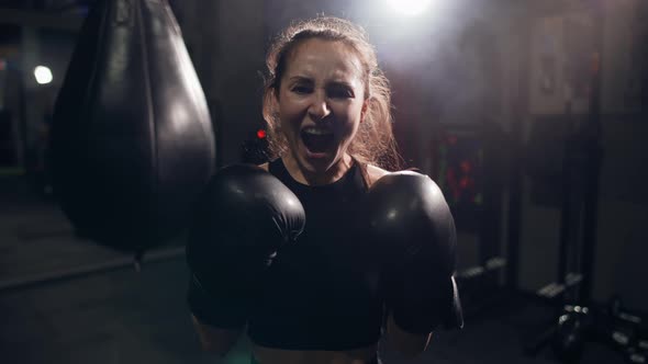 Portrait of Female Boxer Standing at Dark Gym Looking Intensely at the Camera and Screaming