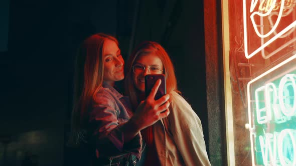 Two Millennial Women Pose on Phone Camera in Neon