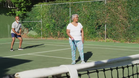 African american senior couple playing tennis on the tennis court on a bright sunny day