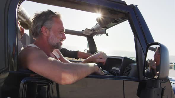 Happy caucasian gay male couple in car admiring the view and pointing on sunny day at the beach