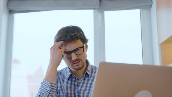 Man in glasses with a surprised look, looks thoughtfully at the monitor screen. Makes calculations.