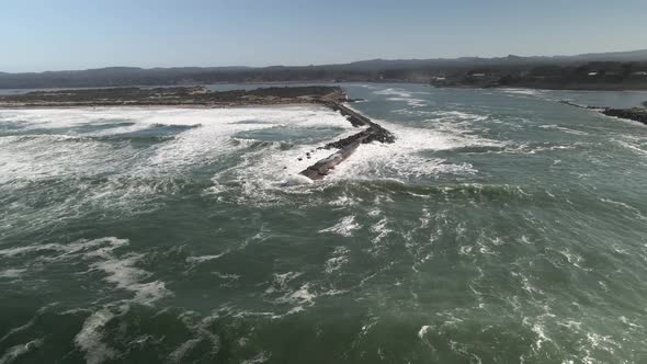 Pulling back as ocean waves crash on the narrow Coquille River jetty, Oregon, aerial