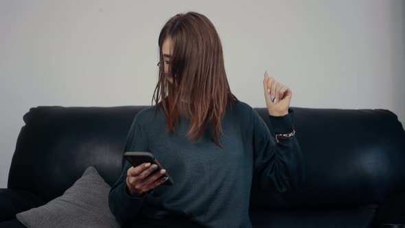 The Portrait of a Redhaired Freckled Girl with Glasses Looks at the Phone Screen and Performs