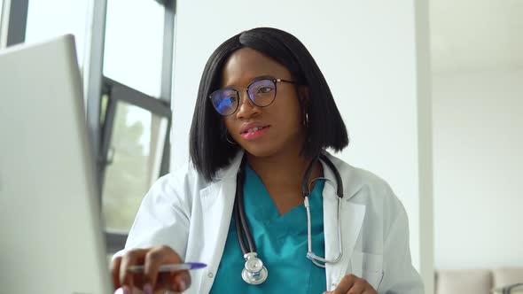Attractive African American Female Doctor Using Laptop at Desk While Working in Medical Office