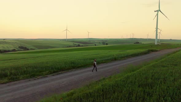 Young tourist with a backpack near a farm with green energy windmills, aerial view