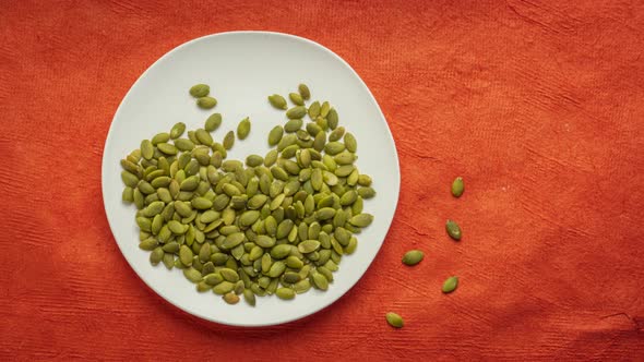 Organic raw pumpkin seeds are falling into white ceramic plate