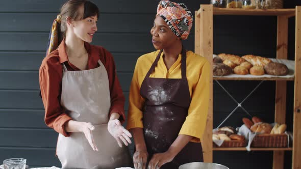 Portrait of Two Cheerful Multiethnic Colleagues Making Dough in Bakery